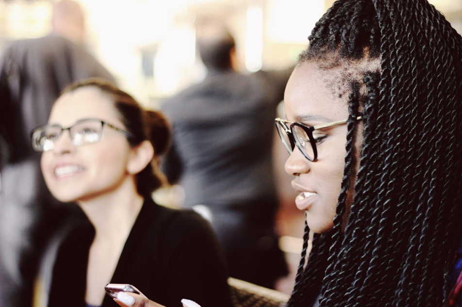 Two women wearing glasses and of different races sit next to each other.